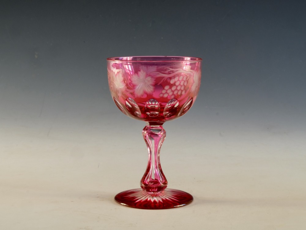 An antique Victorian wine glass featuring a ruby red overlay cut to clear with wheel-engraved grapevine motifs, a faceted stem, and a star-cut foot.