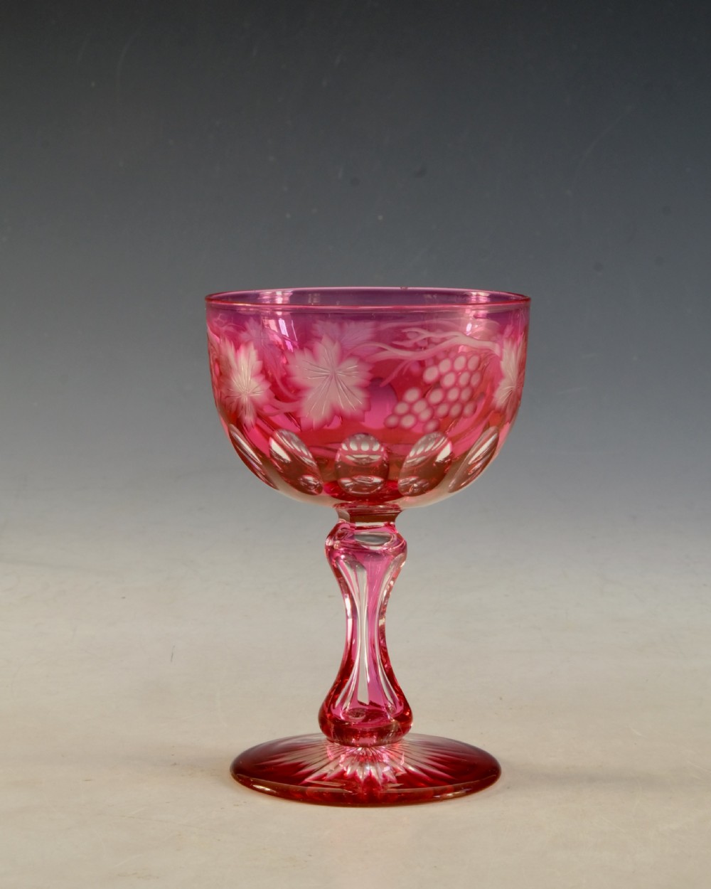 An antique Victorian wine glass featuring a ruby red overlay cut to clear with wheel-engraved grapevine motifs, a faceted stem, and a star-cut foot. View II