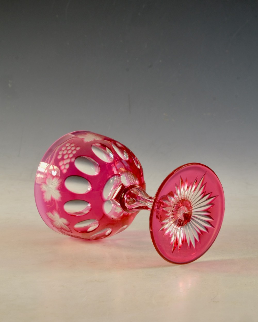 An antique Victorian wine glass featuring a ruby red overlay cut to clear with wheel-engraved grapevine motifs, a faceted stem, and a star-cut foot. View III