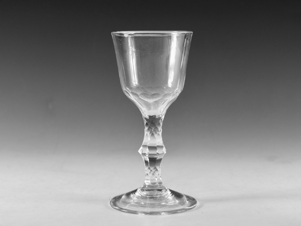 An 18th-century clear lead glass goblet featuring a faceted diamond-cut stem and a round bowl resting on a flat conical foot.