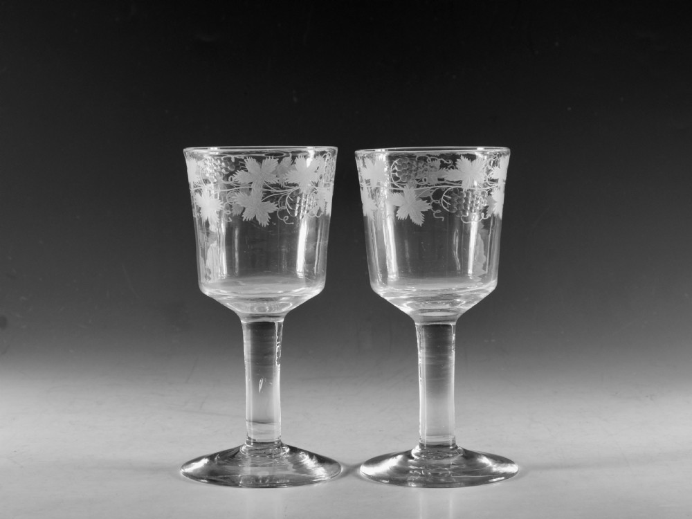 A pair of 18th-century clear lead glass goblets featuring plain straight stems and wheel-engraved grapevine motifs around the rims.