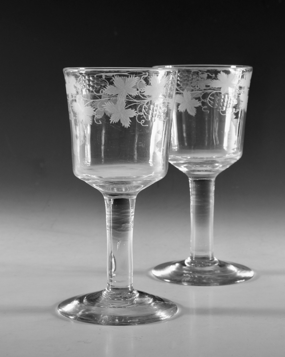 A pair of 18th-century clear lead glass goblets featuring plain straight stems and wheel-engraved grapevine motifs around the rims. View II
