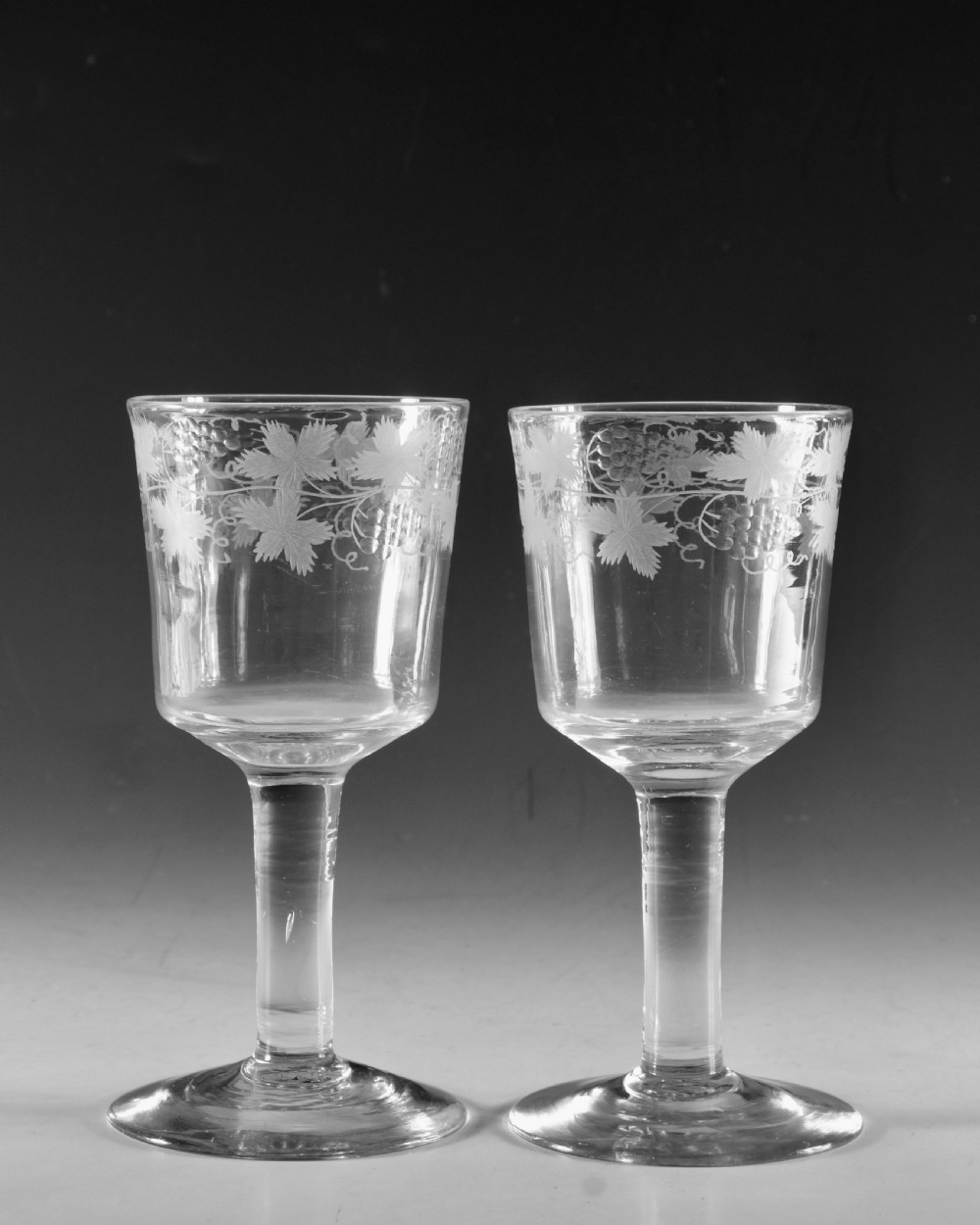 A pair of 18th-century clear lead glass goblets featuring plain straight stems and wheel-engraved grapevine motifs around the rims. View III