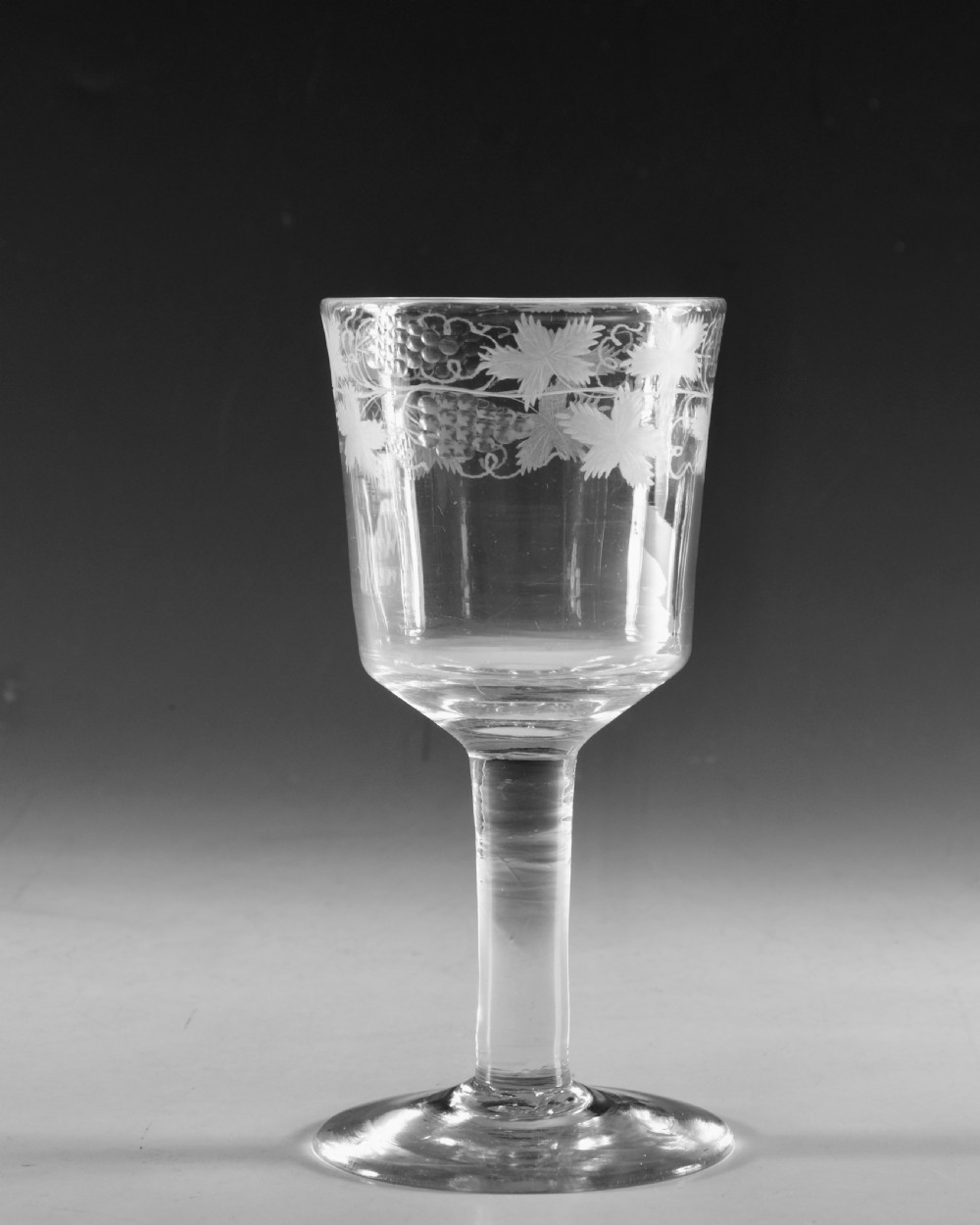A pair of 18th-century clear lead glass goblets featuring plain straight stems and wheel-engraved grapevine motifs around the rims. View V