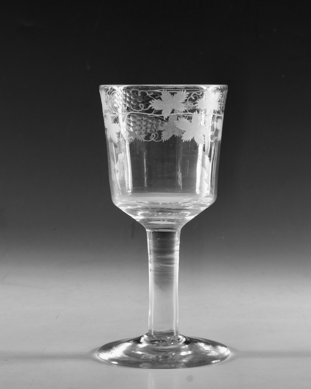 A pair of 18th-century clear lead glass goblets featuring plain straight stems and wheel-engraved grapevine motifs around the rims. View VII
