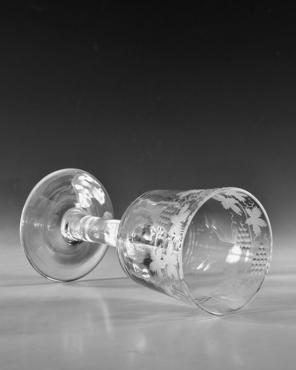 A pair of 18th-century clear lead glass goblets featuring plain straight stems and wheel-engraved grapevine motifs around the rims. View IX