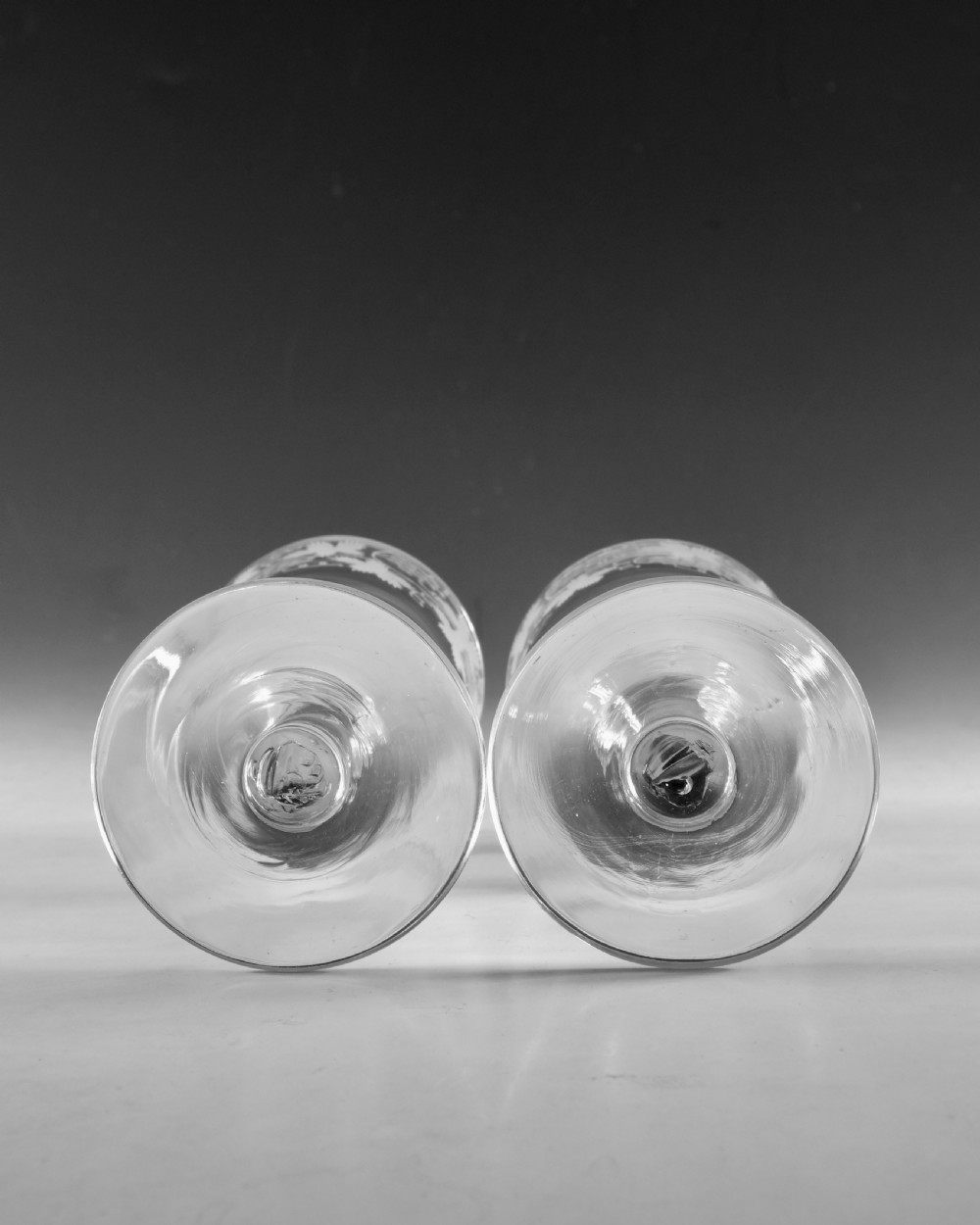A pair of 18th-century clear lead glass goblets featuring plain straight stems and wheel-engraved grapevine motifs around the rims. View X