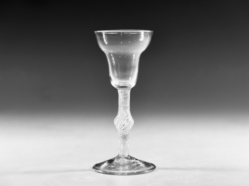 An 18th-century English clear lead glass wine glass featuring a flared bowl, a knopped stem with a multi-spiral air twist pattern, and a wide circular foot.