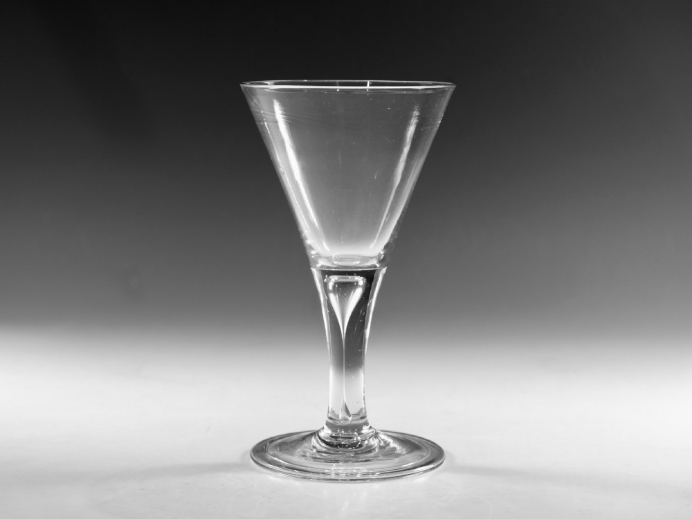 A mid-18th-century clear glass goblet featuring a conical bowl, a plain stem containing an elongated air tear, and a circular conical foot.