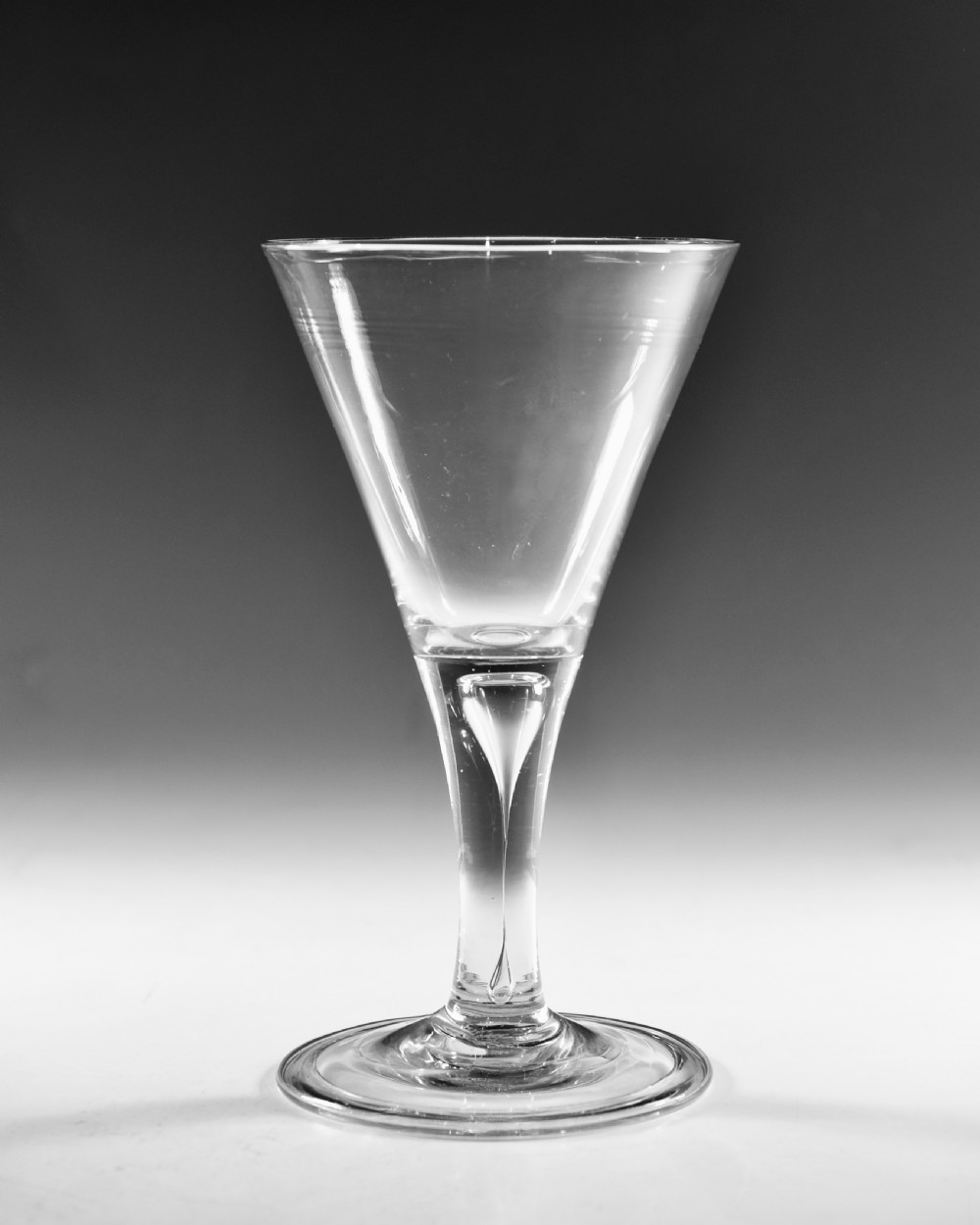 A mid-18th-century clear glass goblet featuring a conical bowl, a plain stem containing an elongated air tear, and a circular conical foot. View III