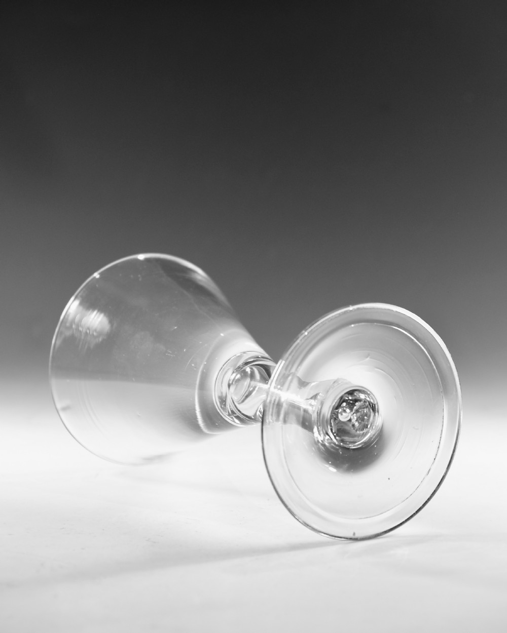 A mid-18th-century clear glass goblet featuring a conical bowl, a plain stem containing an elongated air tear, and a circular conical foot. View V