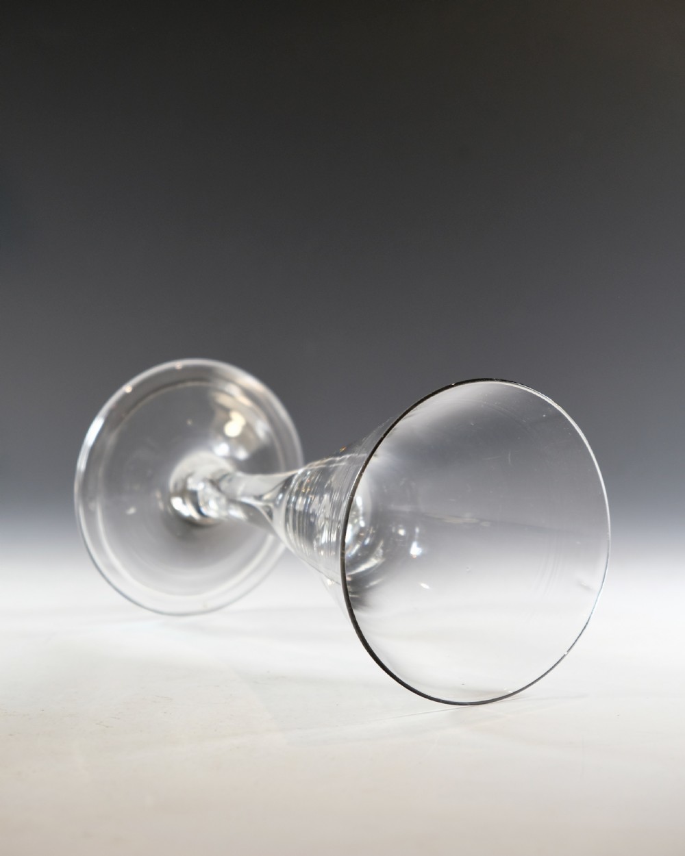 A mid-18th-century clear glass goblet featuring a conical bowl, a plain stem containing an elongated air tear, and a circular conical foot. View VI