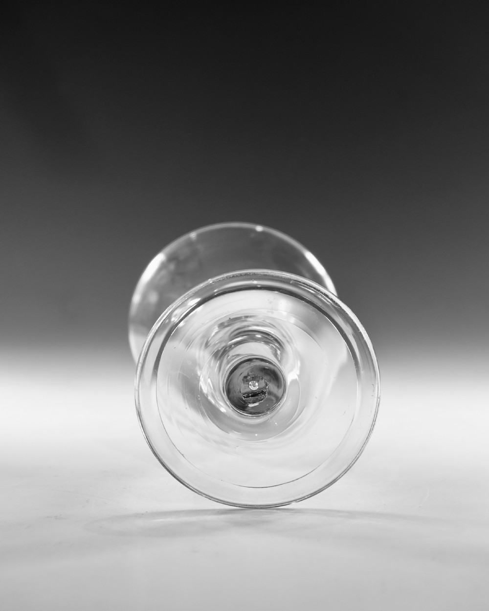 A mid-18th-century clear glass goblet featuring a conical bowl, a plain stem containing an elongated air tear, and a circular conical foot. View VII