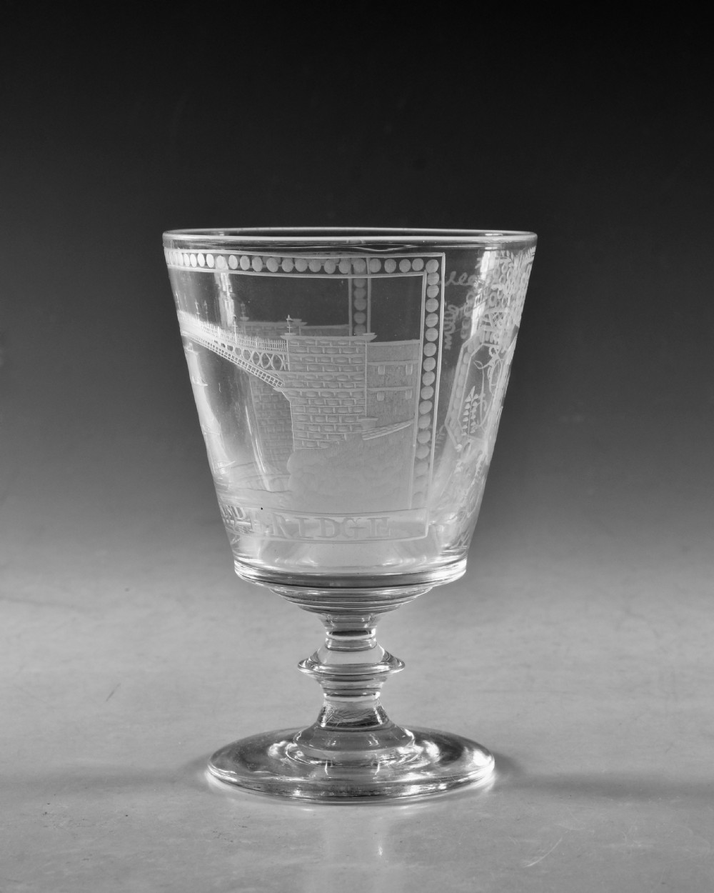 An antique clear glass rummer featuring detailed wheel engraving of a sailing ship beneath the Wearmouth Sunderland Bridge, supported by a knopped stem and circular foot. View V