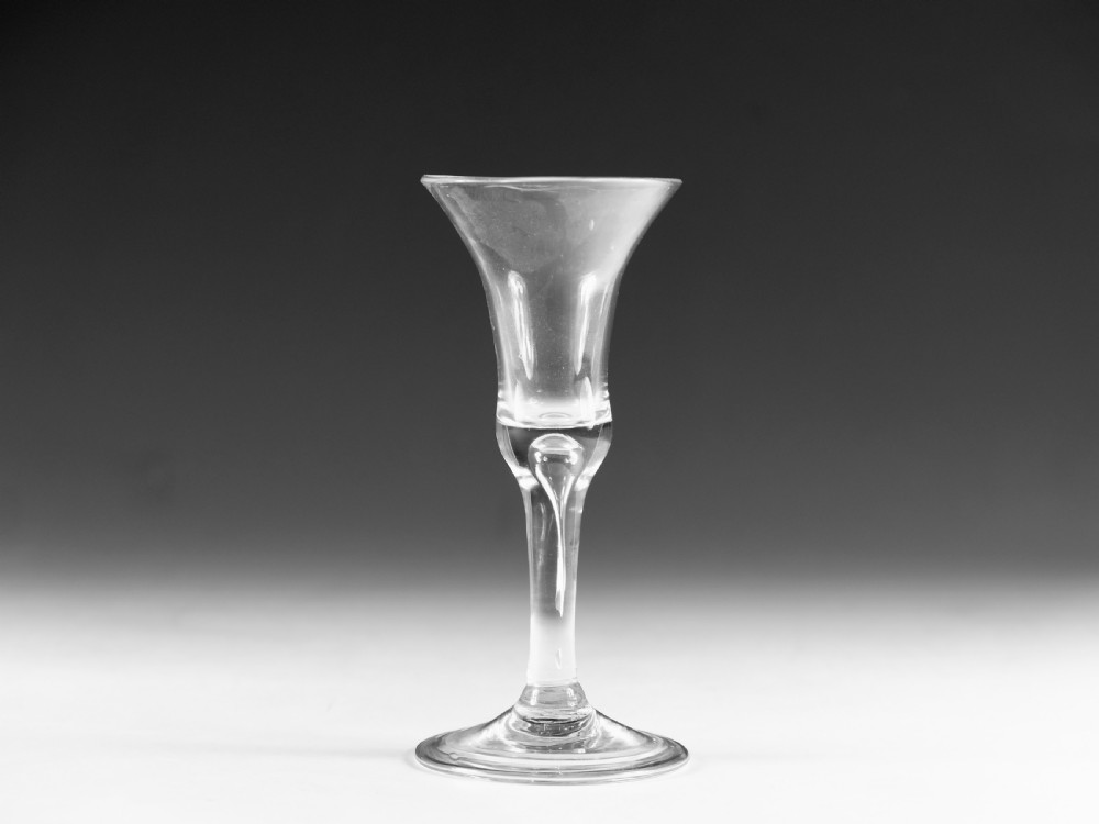 An 18th-century English clear lead glass wine glass featuring a flared bell bowl, a plain stem with a central air tear, and a circular conical foot.