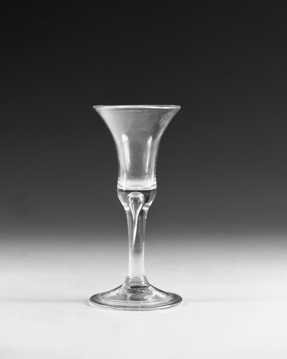 An 18th-century English clear lead glass wine glass featuring a flared bell bowl, a plain stem with a central air tear, and a circular conical foot. View II