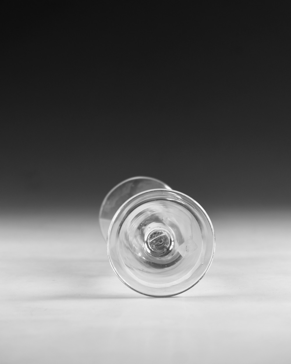 An 18th-century English clear lead glass wine glass featuring a flared bell bowl, a plain stem with a central air tear, and a circular conical foot. View V