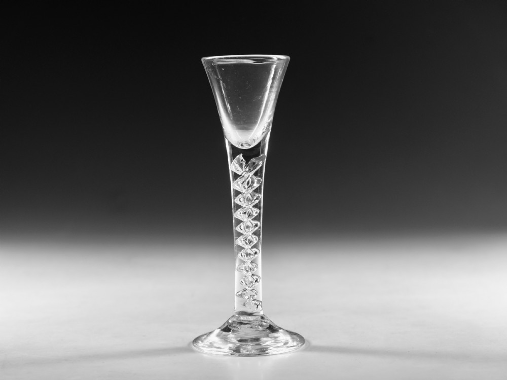 An antique clear lead glass cordial glass featuring a flared funnel bowl, a central mercury air-twist stem, and a wide conical base.