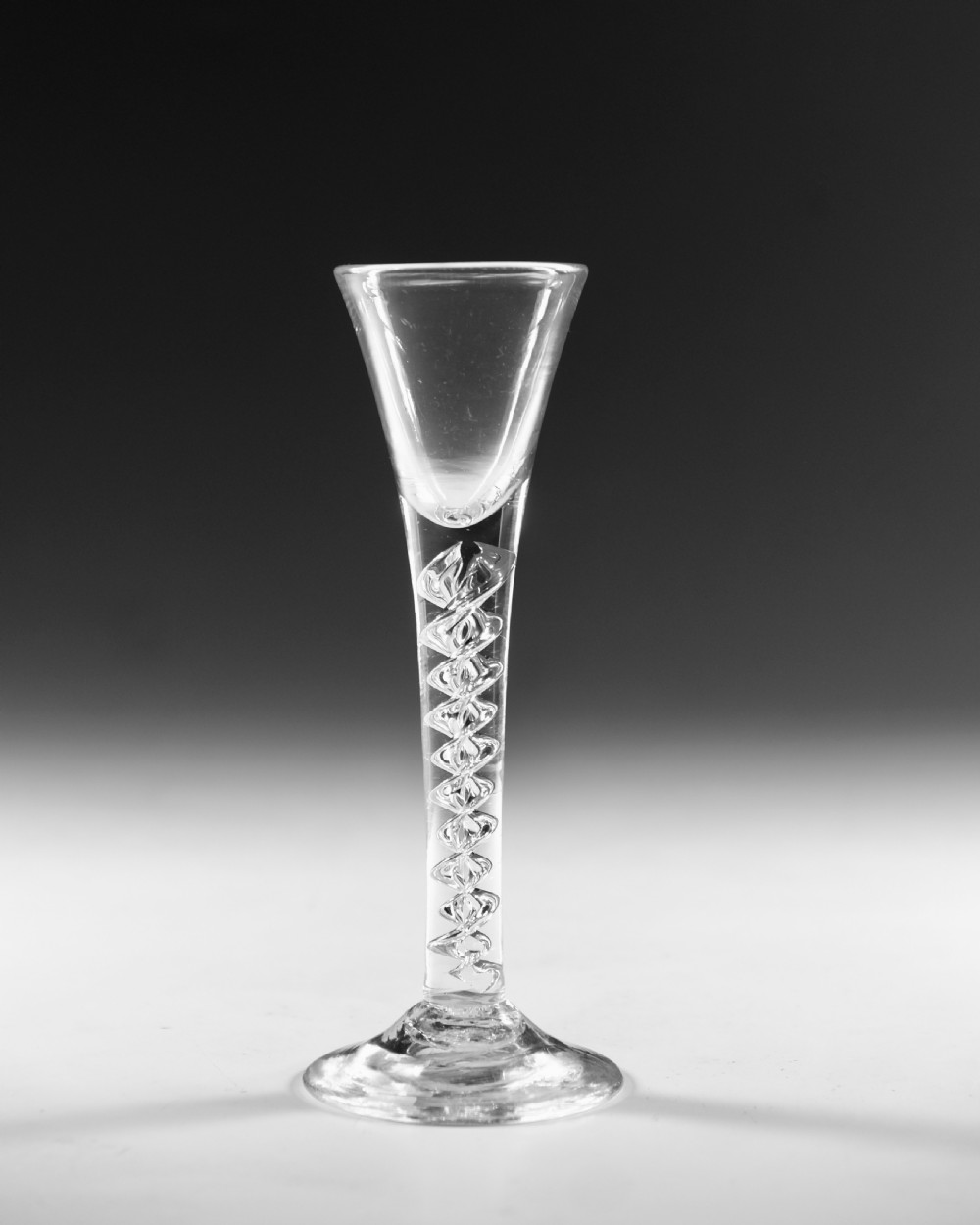 An antique clear lead glass cordial glass featuring a flared funnel bowl, a central mercury air-twist stem, and a wide conical base. View II