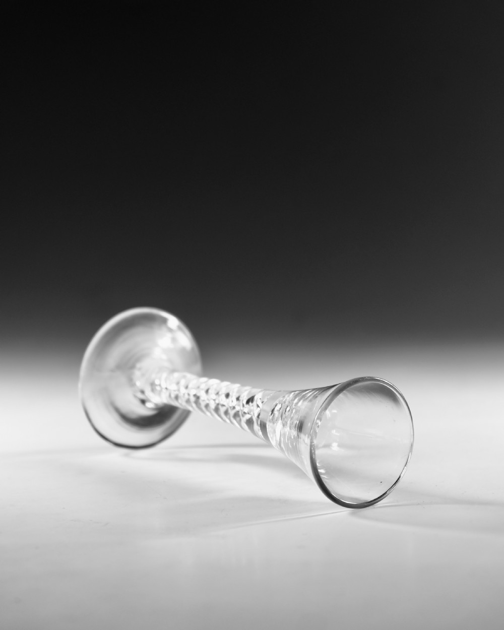 An antique clear lead glass cordial glass featuring a flared funnel bowl, a central mercury air-twist stem, and a wide conical base. View IV