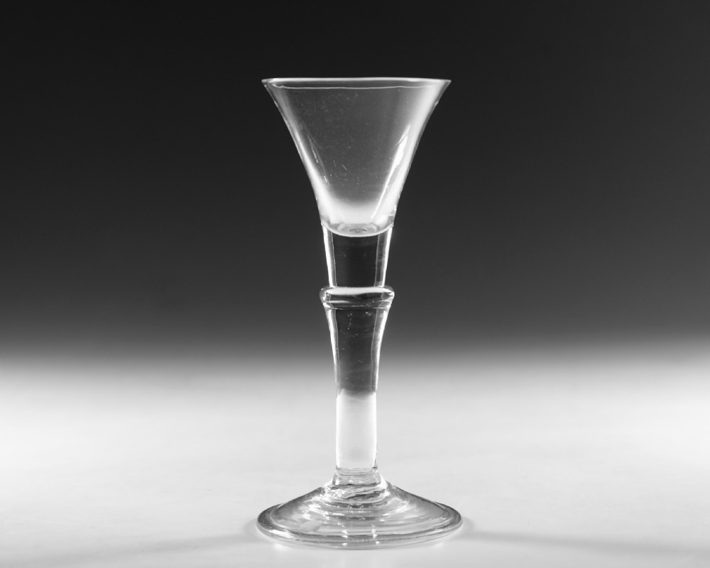 An eighteenth-century clear glass wine glass featuring a flared funnel bowl, a central stem knop, and a conical foot.