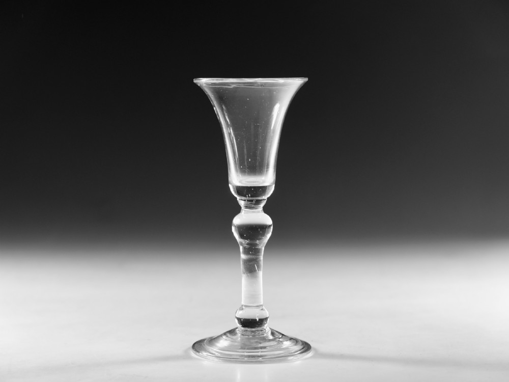 A Georgian clear glass wine glass featuring a flared bell bowl, a knopped stem, and a circular conical foot.