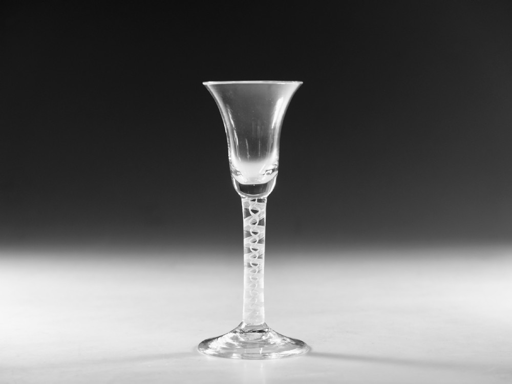 A Georgian clear glass wine goblet with a flared bell bowl and an opaque white spiral twist stem on a circular conical foot.