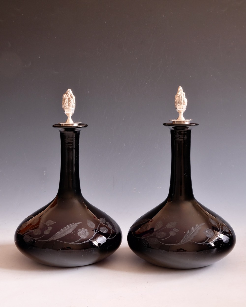 A pair of dark amethyst glass decanters featuring wheel-engraved botanical motifs and topped with silver flame-shaped stoppers. View III