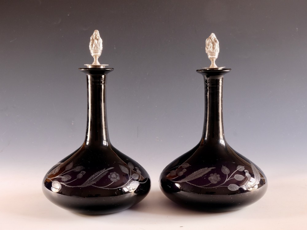 A pair of dark amethyst glass decanters featuring wheel-engraved botanical motifs and topped with silver flame-shaped stoppers. View IX