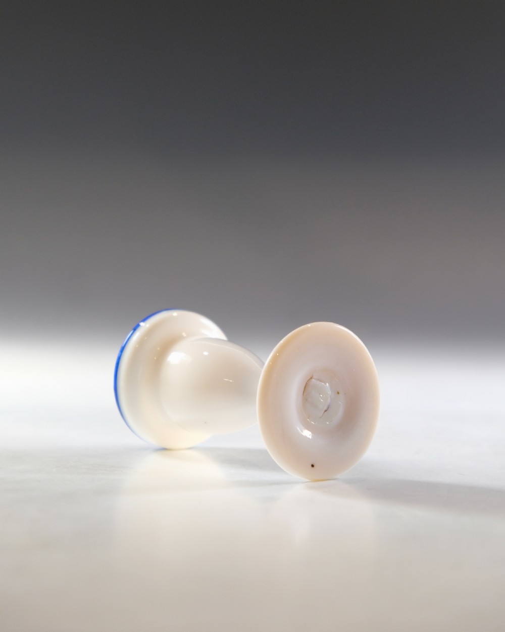 An opaque white glass egg cup featuring a cobalt blue rim on a narrow pedestal stem and flared circular base. View III