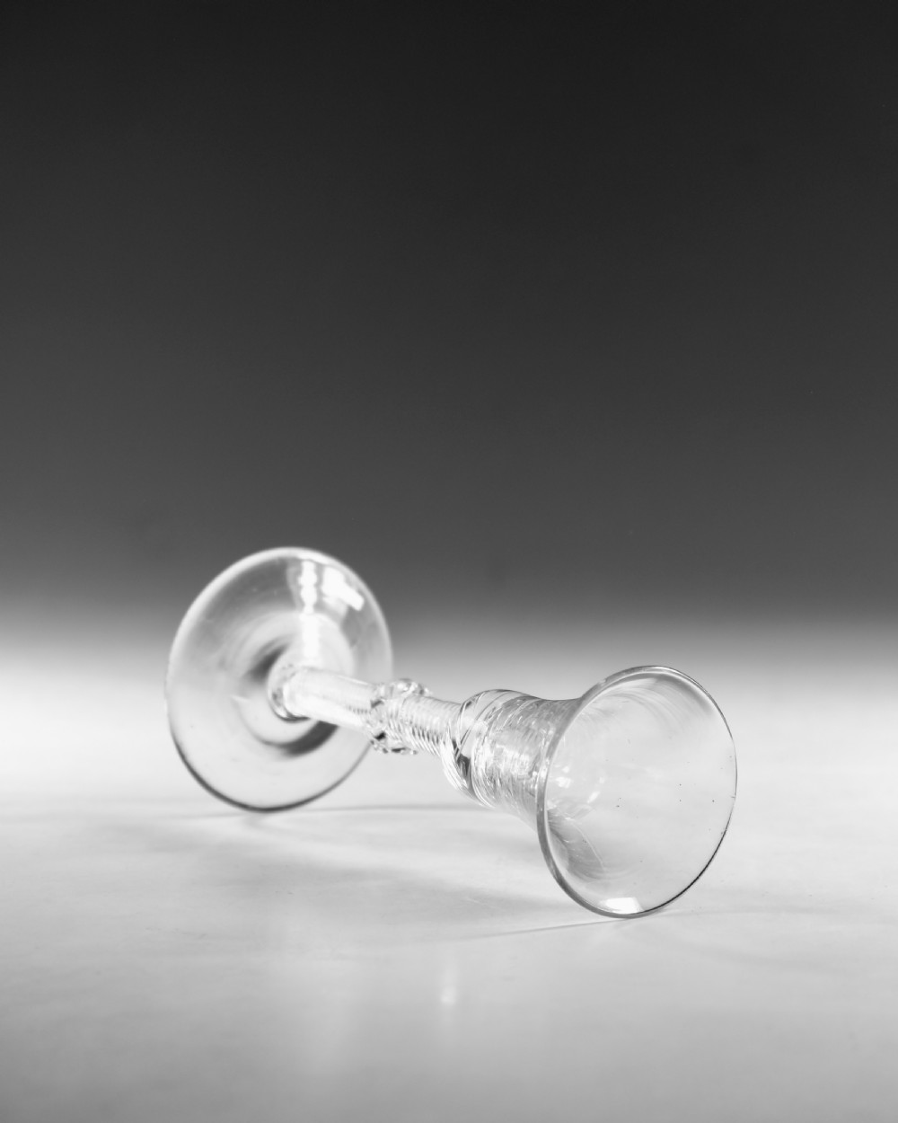 An 18th-century clear glass wine vessel featuring a flared bell bowl, an intricate air-twist stem with a central knop, and a flat conical base. View V