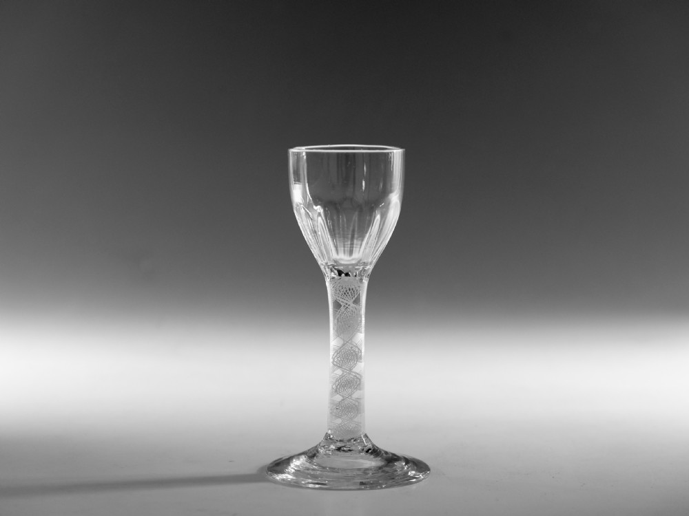 An 18th-century clear glass wine vessel featuring a rounded fluted bowl, an opaque white twist stem, and a conical foot.