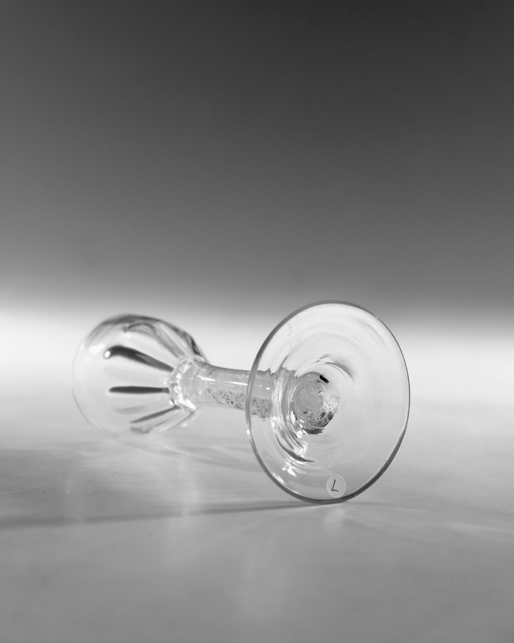 An 18th-century clear glass wine vessel featuring a rounded fluted bowl, an opaque white twist stem, and a conical foot. View V