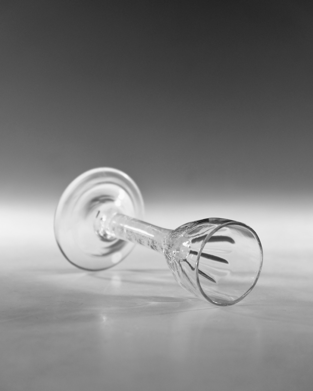 An 18th-century clear glass wine vessel featuring a rounded fluted bowl, an opaque white twist stem, and a conical foot. View VI