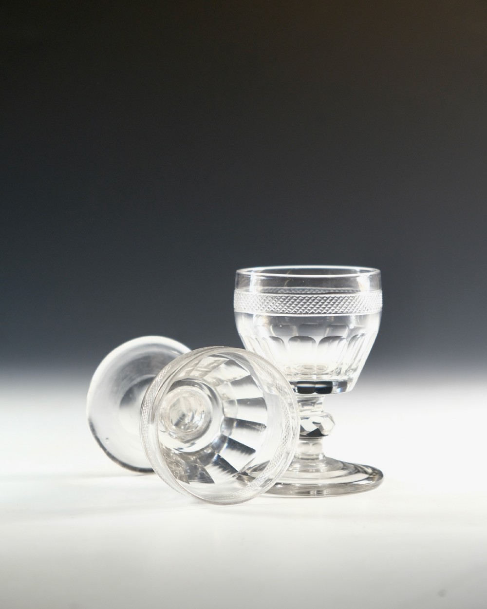 A set of seven clear Georgian cut glass port glasses featuring diamond-patterned bands and faceted stems. View VII