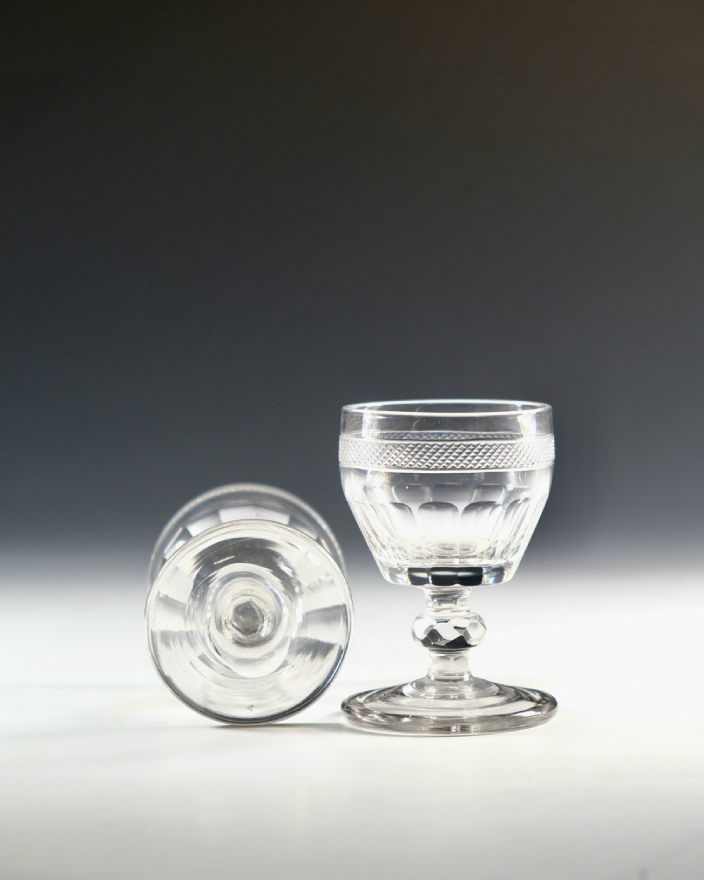 A set of seven clear Georgian cut glass port glasses featuring diamond-patterned bands and faceted stems. View VIII