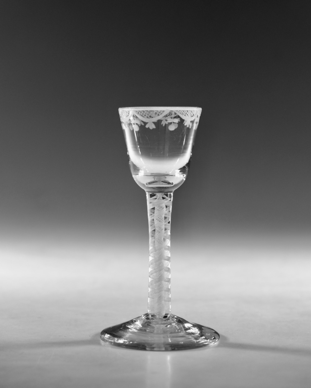 An 18th-century Georgian clear lead glass wine glass featuring an engraved bowl rim, an opaque twist stem, and a circular conical foot. View II