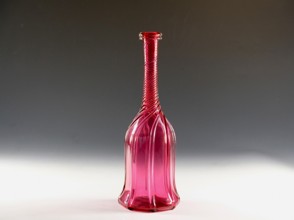 An antique English cranberry red glass serving bottle with a spiralled neck and a fluted lobed body.