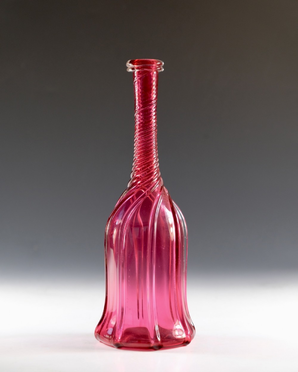An antique English cranberry red glass serving bottle with a spiralled neck and a fluted lobed body. View II