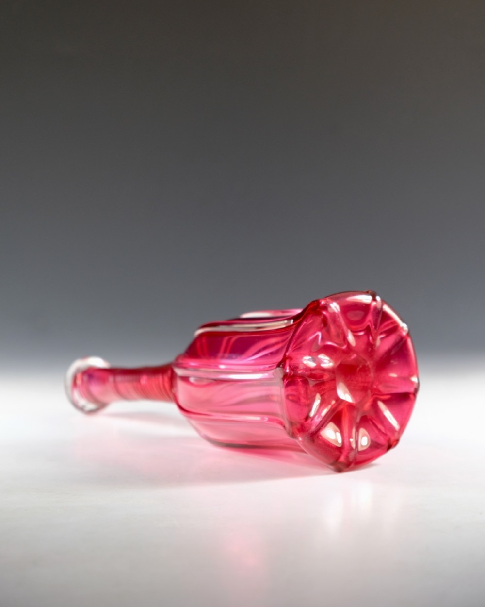 An antique English cranberry red glass serving bottle with a spiralled neck and a fluted lobed body. View III
