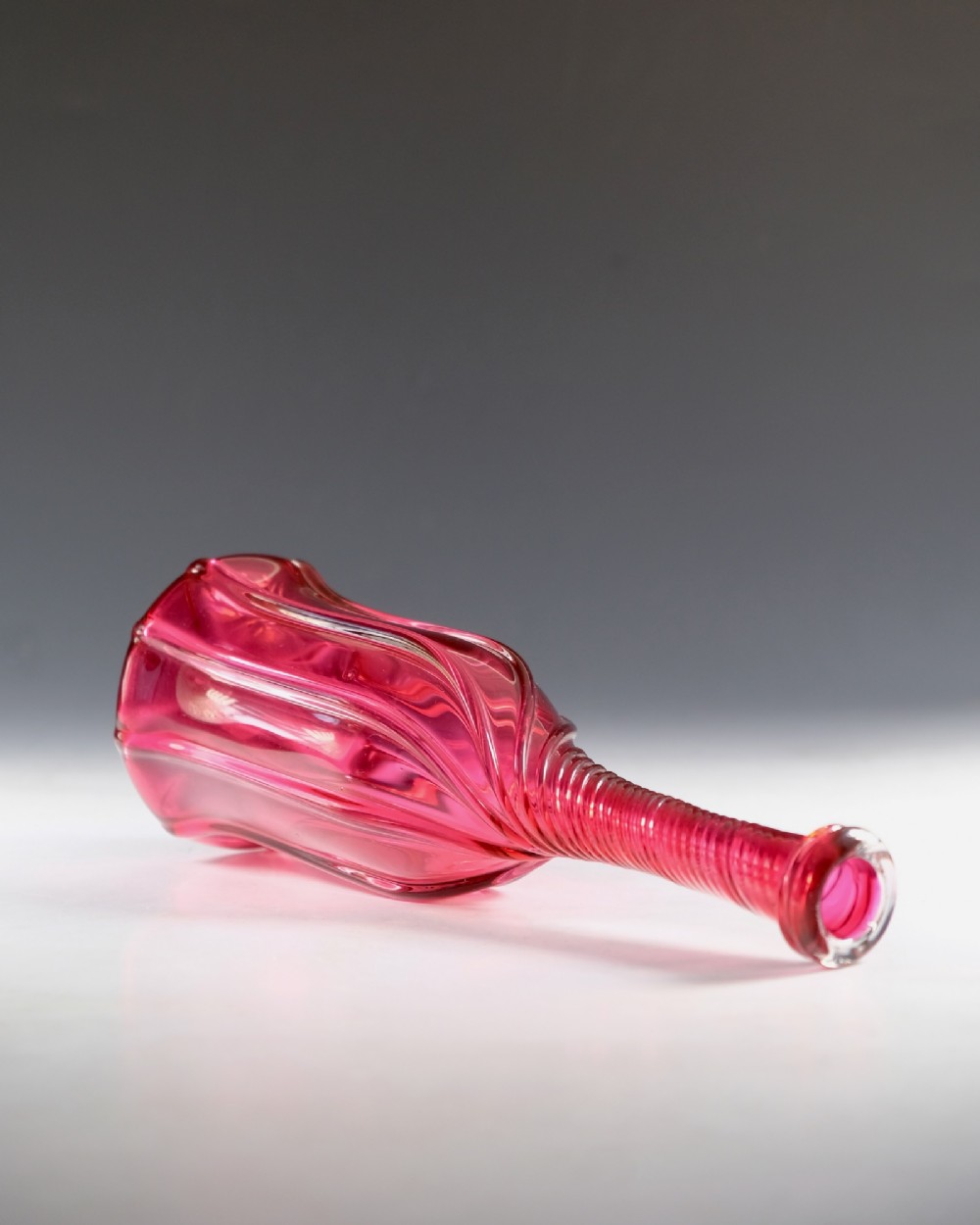 An antique English cranberry red glass serving bottle with a spiralled neck and a fluted lobed body. View IV