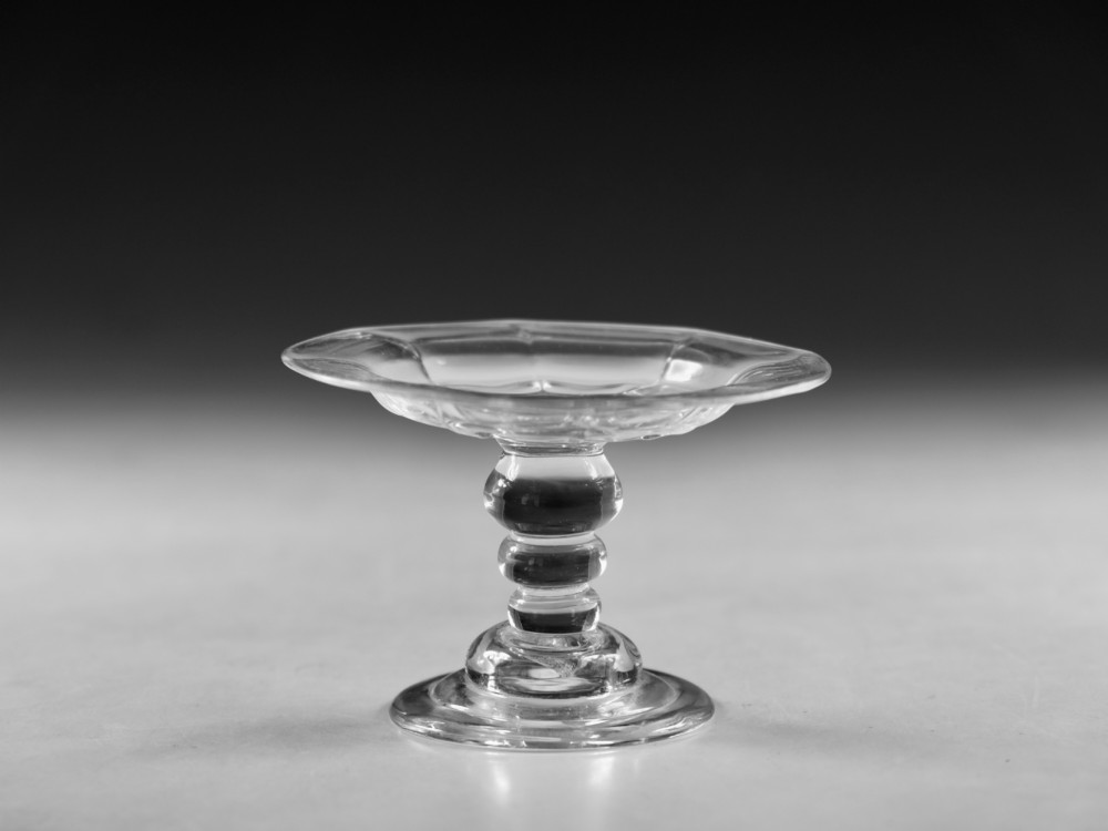 An eighteenth-century Georgian clear lead glass patch stand featuring a shallow rimmed top, a multi-knopped baluster stem, and a circular folded foot.