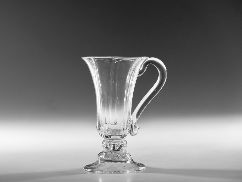 An 18th-century clear glass jelly vessel featuring a fluted bell-shaped bowl, a single side handle, a knopped stem element, and a circular foot.