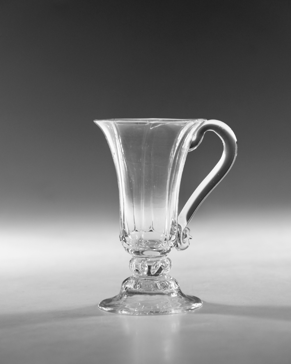 An 18th-century clear glass jelly vessel featuring a fluted bell-shaped bowl, a single side handle, a knopped stem element, and a circular foot. View II