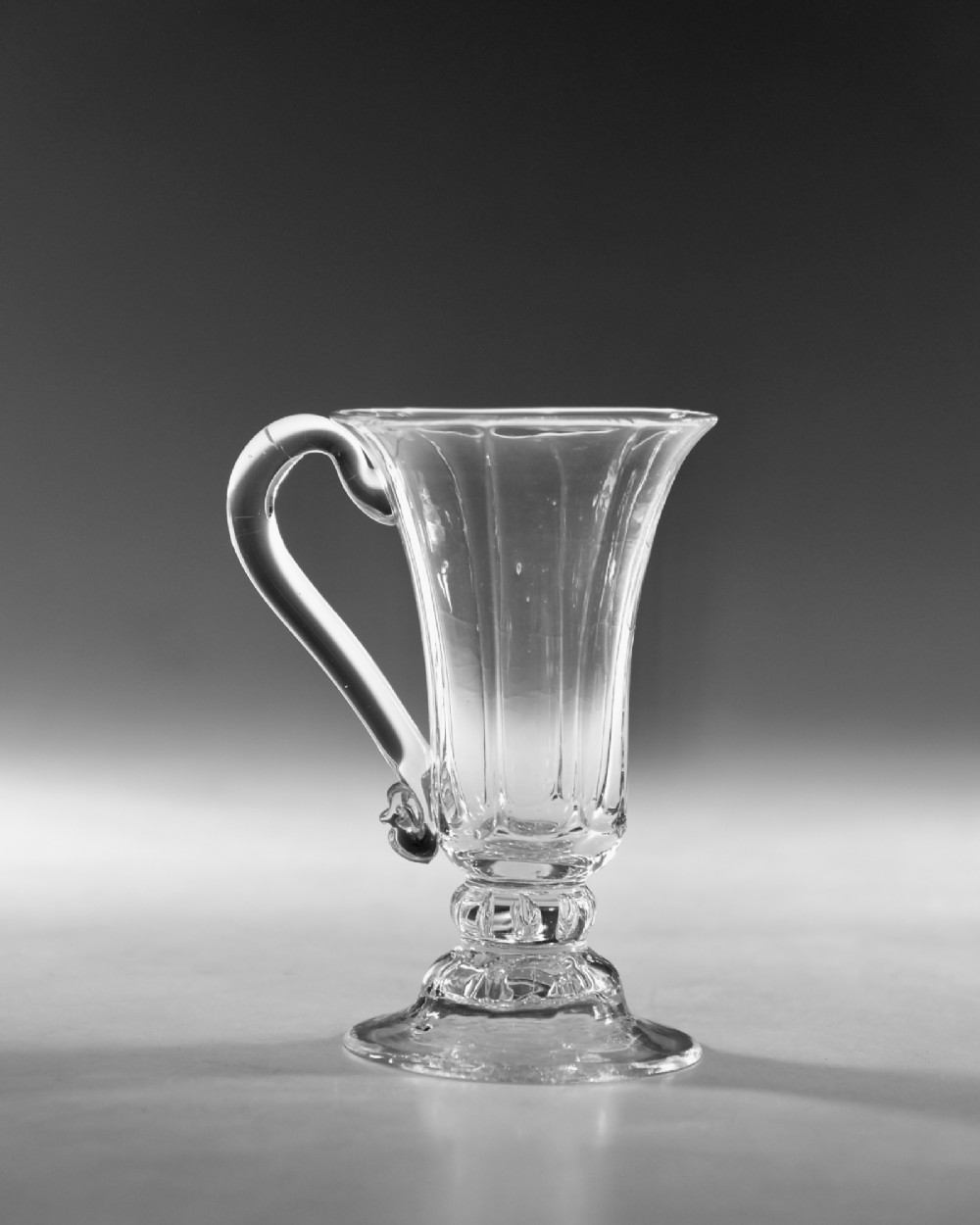 An 18th-century clear glass jelly vessel featuring a fluted bell-shaped bowl, a single side handle, a knopped stem element, and a circular foot. View III