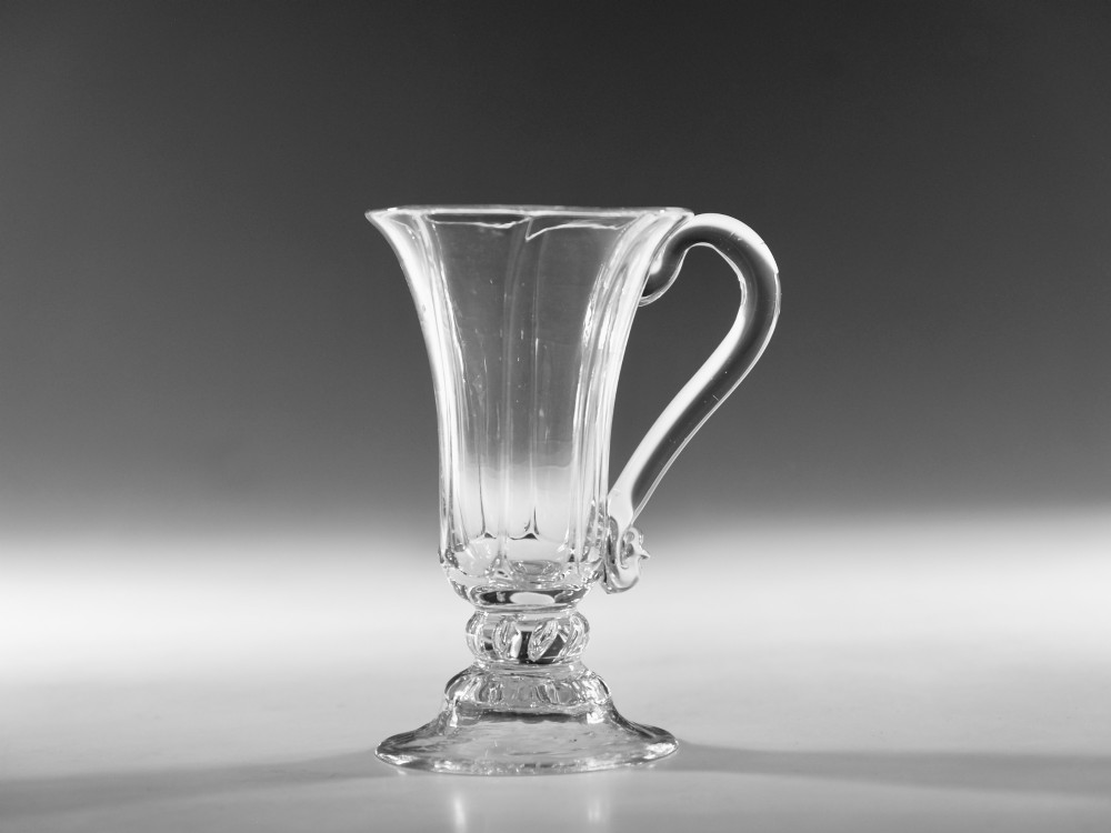 An 18th-century clear glass jelly vessel featuring a fluted bell-shaped bowl, a single side handle, a knopped stem element, and a circular foot. View VII