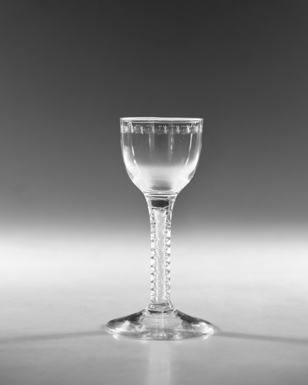A clear glass wine goblet featuring a wheel-engraved rim pattern, an air twist stem, and a flat conical foot, dating to circa 1755. View II