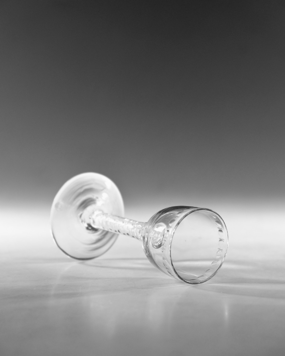 A clear glass wine goblet featuring a wheel-engraved rim pattern, an air twist stem, and a flat conical foot, dating to circa 1755. View V