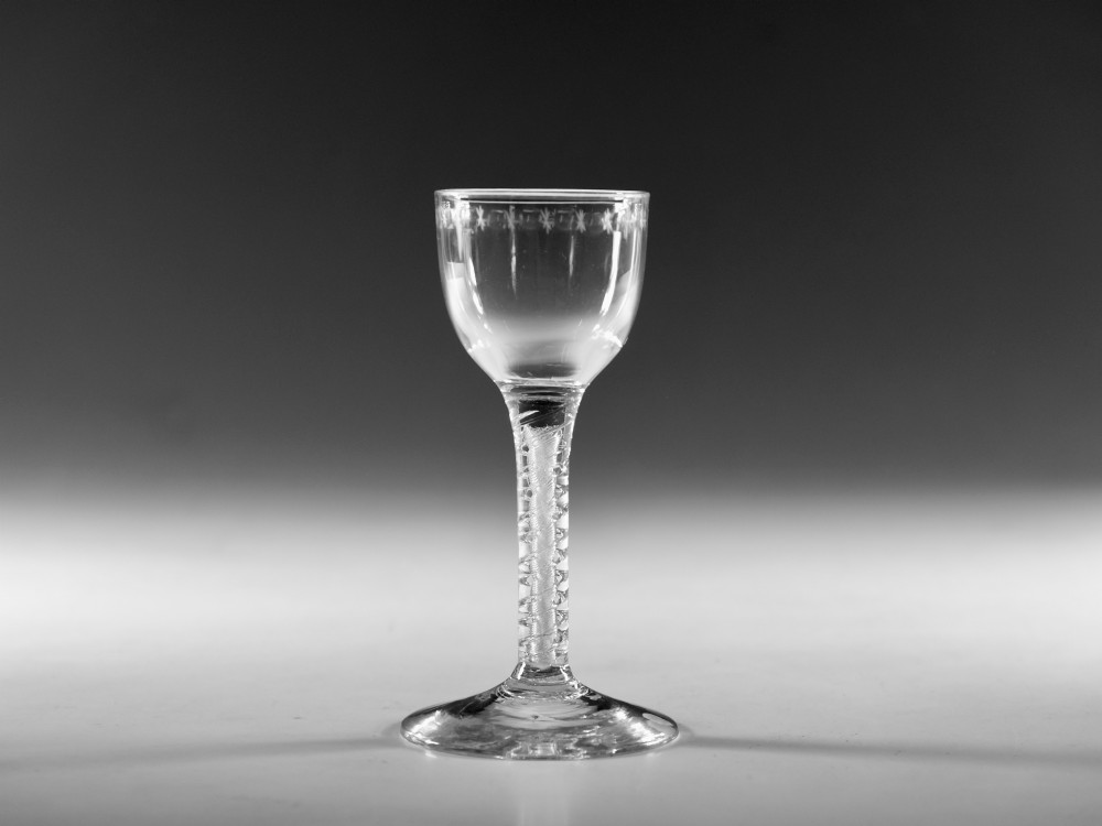 A clear glass wine goblet featuring a wheel-engraved rim pattern, an air twist stem, and a flat conical foot, dating to circa 1755. View VII