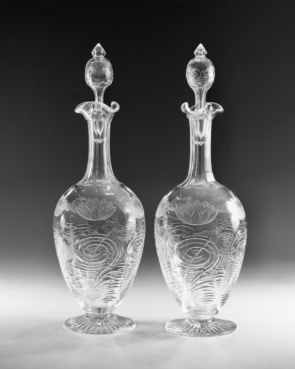 A pair of antique clear glass decanters with intaglio water lily engravings, tall slender necks, and matching glass stoppers. View II
